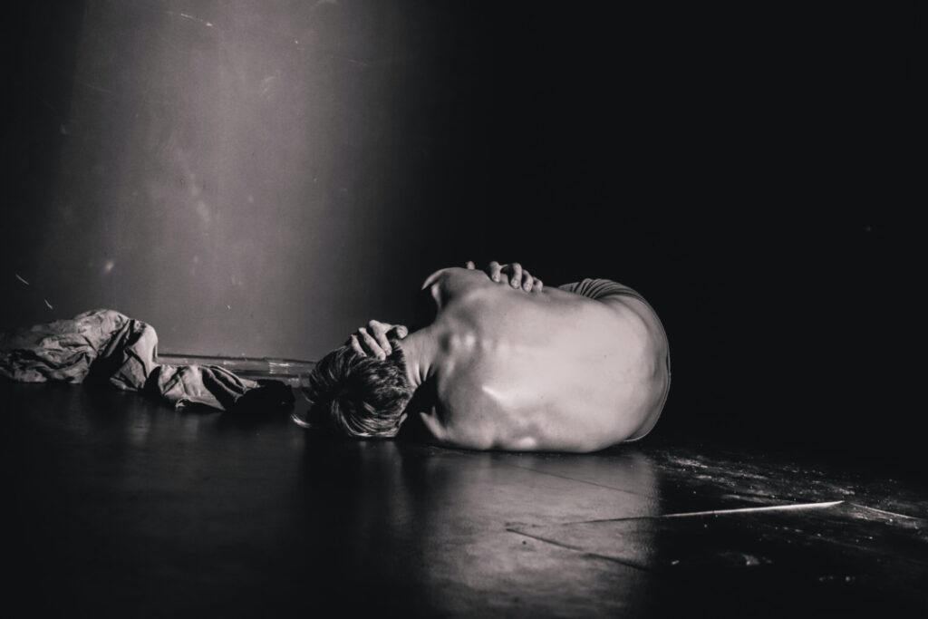Ein schwarz-weiß Bild eines Mannes, der vor Fibromyalgie-Schmerzen verkrampft auf dem Boden liegt.
