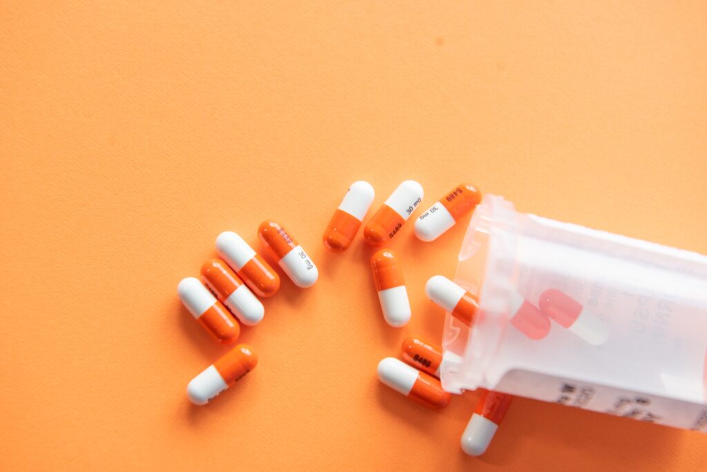 Mehrere organe-weiße Pillen die aus einer Dose auf eine orangene Fläche geschüttet werden