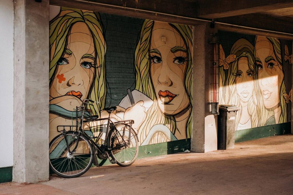 Ein Rad lehnt gegen eine Wand mit Street Art in Form verschiedener Frauengesichter